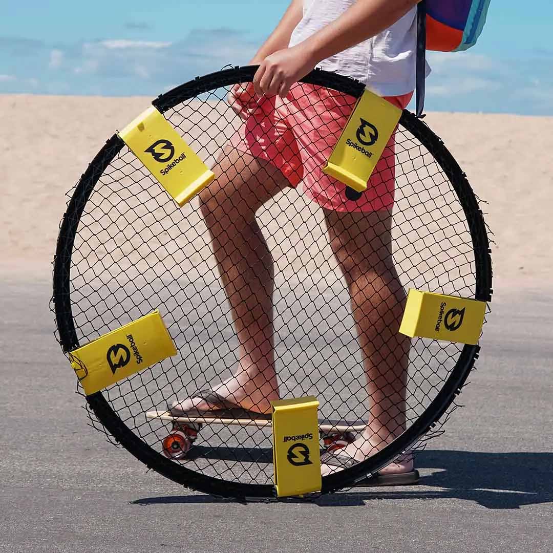 A guy on a skateboard carrying the Spikeball Set with ease