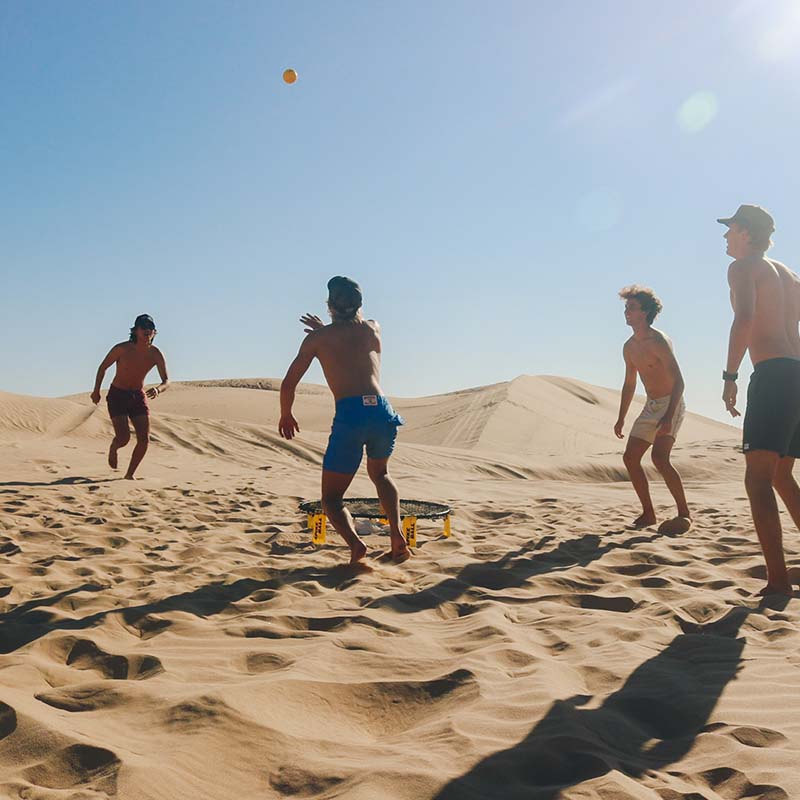 A group of guys playing Spikeball in the middle of the desert