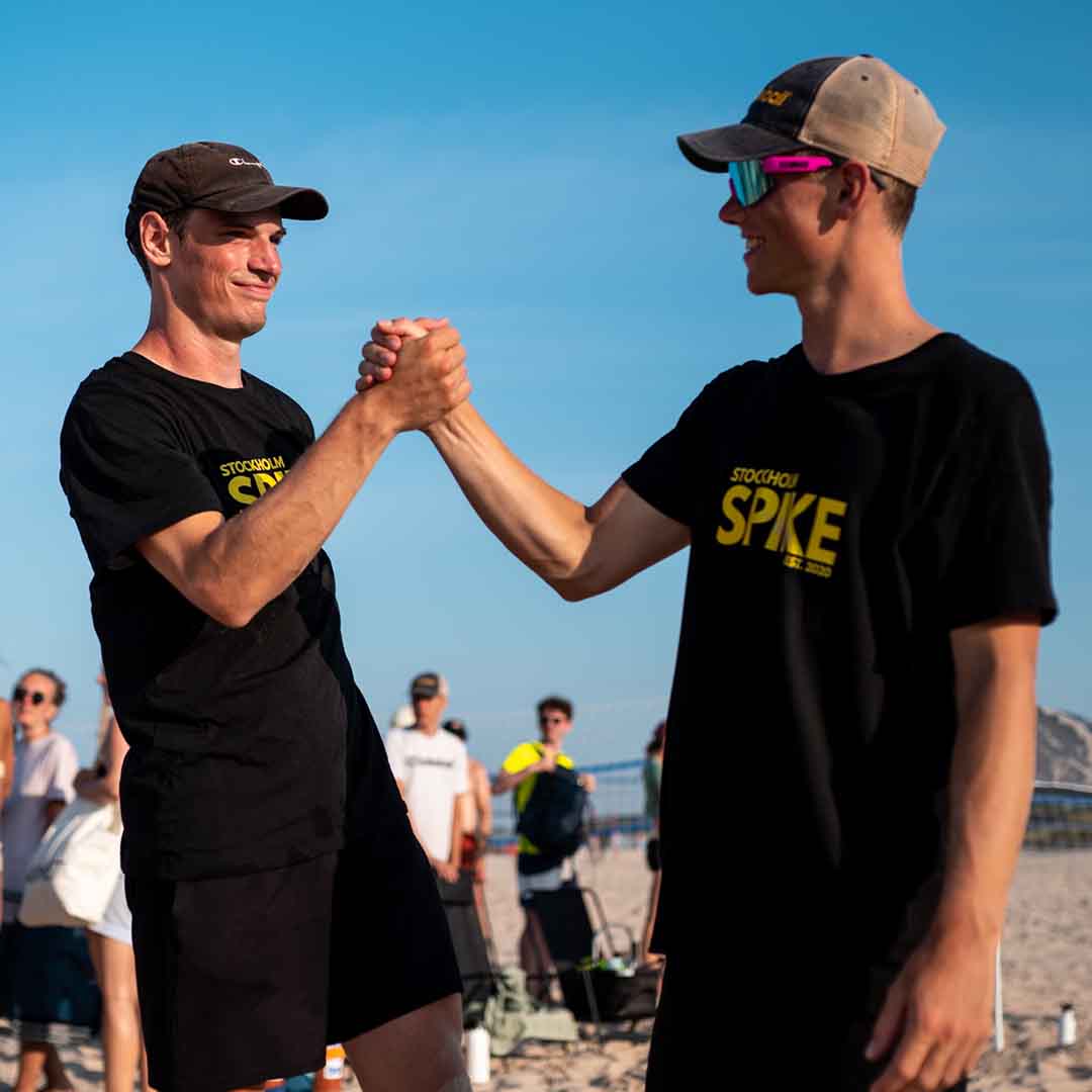 Two men shaking hands on the beach playing spikeball